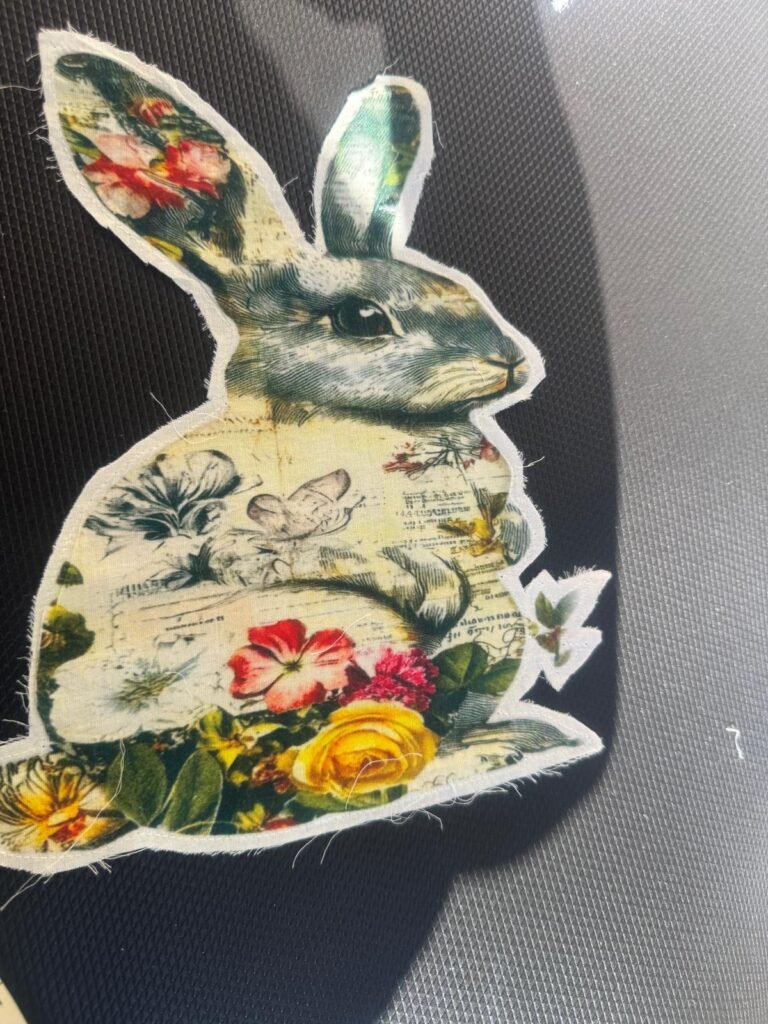 This is a vintage-style decorative rabbit cutout or sticker, featuring a collage design with floral and textual elements. embroidered patch or appliqué
