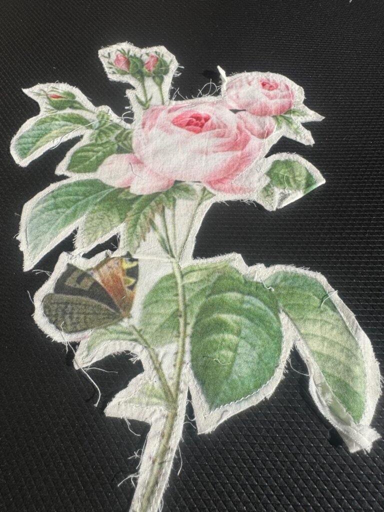 The image is a fabric appliqué featuring a botanical illustration of pink roses and a butterfly. embroidered patch or appliqué