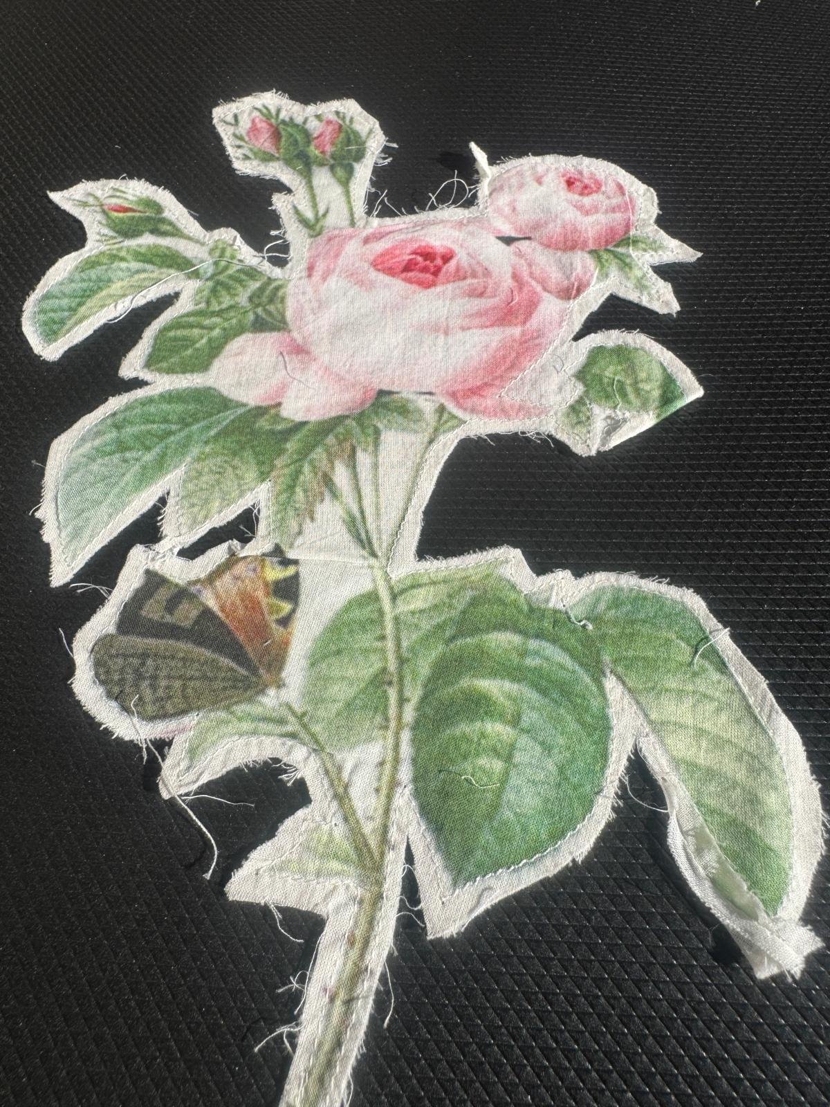 The image is a fabric appliqué featuring a botanical illustration of pink roses and a butterfly. embroidered patch or appliqué